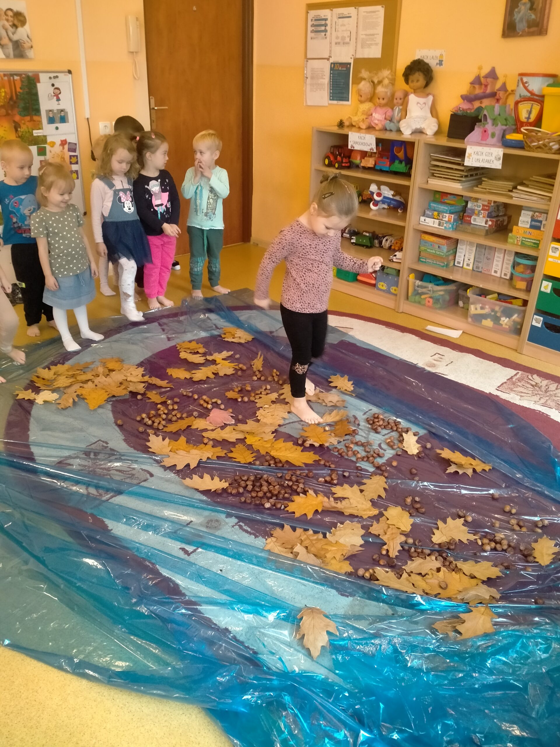 grupa dzieci boso chodzi po dywanie z żółędzi i liści